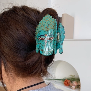 Détail d'une pince à cheveux en acétate vert au design Bouddha portée sur les cheveux