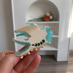 Détail de la pince à cheveux en acétate en forme d'oiseau avec des motifs bleu et crème