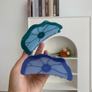 Détail de grandes pinces à cheveux en acétate au design bicolore de feuille de lotus