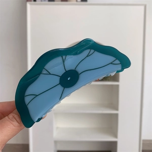 Détail d'une pince à cheveux en acétate en forme de lotus avec texture bleue et verte