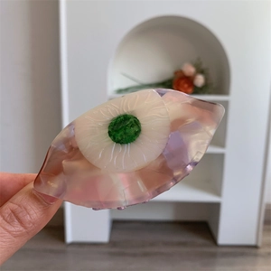 Détail d'une pince à cheveux en acétate en forme d'œil, tons violet et vert créatif
