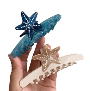 Pinze per capelli a forma di stella marina in acetato blu e beige tenute in mano