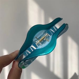 Détail d'une grande pince à cheveux ondulée bleu paon avec ressort en métal doré