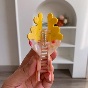 Dettaglio della molletta per capelli in acetato con parte superiore gialla e texture rosa