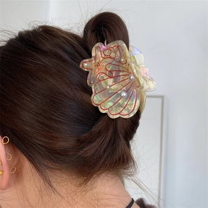 Close-up of a shell-shaped acetate hair claw with iridescent finish and pearls on dark hair