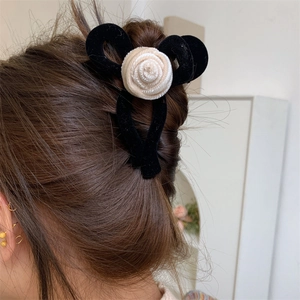 Detail view of a black velvet bow hair claw with a beige knit rose on brown hair