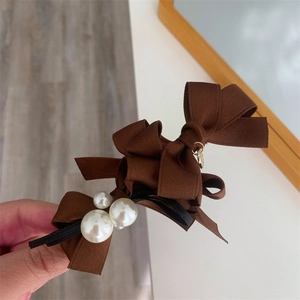 Detail of coffee brown satin bow hair clip with decorative pearls on a metal spring base