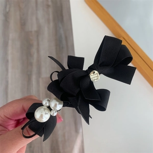 Detail view of a black ribbon bow hair clip with white pearls and a golden charm