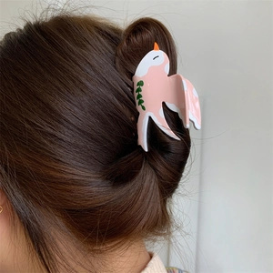 Gros plan sur une pince à cheveux oiseau rose et blanche avec détail de feuille verte