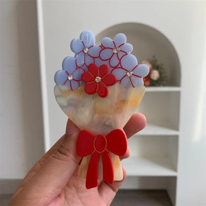 Dettaglio del fermaglio per capelli in acetato con fiori blu, fiocco rosso e strass lucidi