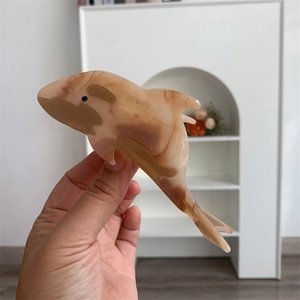 Handheld view of a large acetate whale-shaped hair claw clip with amber marble texture