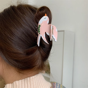 Détail d'une pince à cheveux en forme d'oiseau rose en acétate portée sur une coiffure