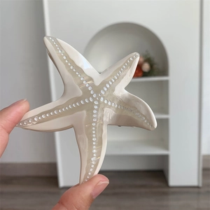 Gros plan d'une pince à cheveux étoile de mer au fini nacré blanc crème et points texturés