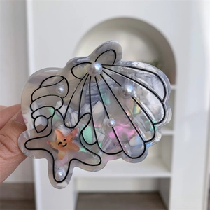Detail of acetate claw clip featuring seashell, conch, and starfish with pearl accents