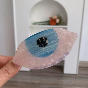 Gros plan d'une pince à cheveux en acétate en forme d'œil avec iris bleu et base rose