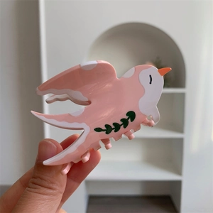 Détail de la pince à cheveux oiseau rose avec pois blancs et motif de feuilles vertes
