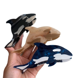 Orca shaped acetate hair claws in black, deep blue, and beige colors on white background