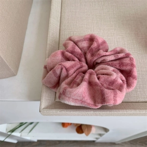 Chouchou à carreaux roses en tricot épais présenté sur un support beige texturé