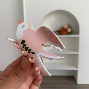 Détail de la pince à cheveux en acétate en forme d'oiseau rose et blanc à motifs