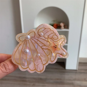 Detailed macro view of seashell and starfish hair claw with pink marble texture and pearls
