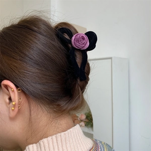 Detail view of a velvet flower hair claw and gold hoop earrings on a female model