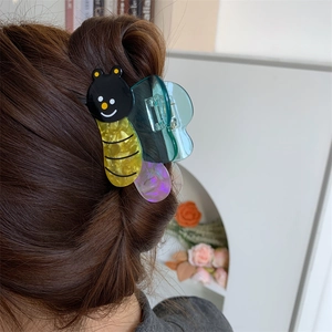 Detailed close-up of a cute bee-shaped hair claw clip with yellow shell texture in brown hair