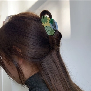 Detail view of a pineapple-shaped hair claw clip in green and yellow on dark brown hair
