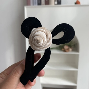 Detail of elegant velvet hair claw featuring a black bow and cream fabric rose flower