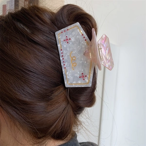 Detail of white marble acetate hair claw clip with pink rhinestones on dark brown hair
