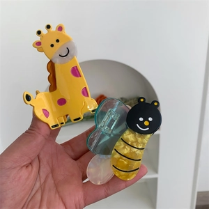 Detail view of cute cartoon giraffe and bee acetate hair claws held in hand