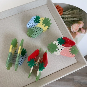 Detail view of strawberry-shaped hair claws in various colors on a textured cream tray