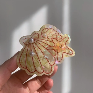 Detail of shell and starfish acetate hair claw with faux pearls and smiley face