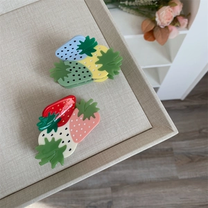 Close-up of strawberry hair claws in pink and green on a beige display plate