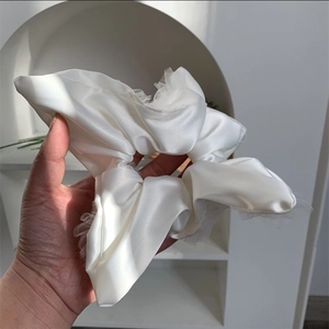 Close-up of pearl white satin scrunchie with lace edge held to show volume and texture