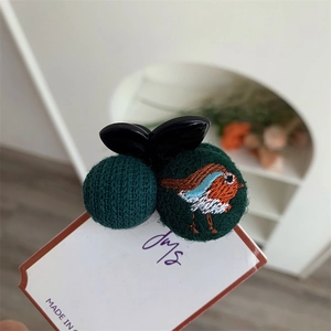 Detail of embroidered bird pattern on a dark green fabric ball and knitted hair clip