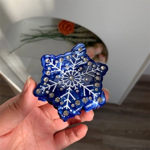 Détail d'une pince à cheveux bleue en forme de flocon avec strass et motifs blancs