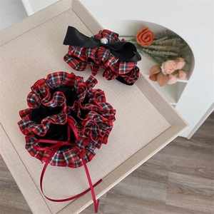 Detailed view of red and black plaid fabric hair scrunchie with bow and pearl detail