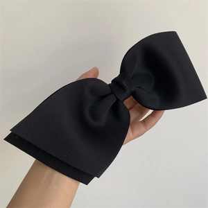 Detailed close-up of a large black textured bow hair clip held by hand for size context