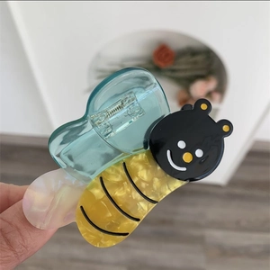 Detail view of cute bee hair claw clip made of textured yellow acetate with blue wings