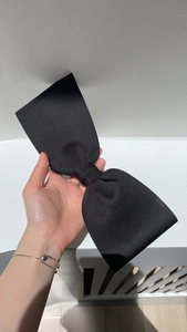 Close-up of a large black satin bow hair clip held by hand to show its soft texture