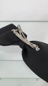 Detail view of the silver metal spring clip and black fabric texture on the bow hairpin