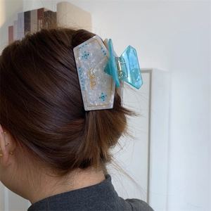Detail of marble acetate hair claw clip with blue rhinestones worn on a hair bun