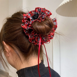 Close-up of a festive plaid hair scrunchie with red ribbons on a dark brown hair bun