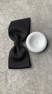 Detail view of large black bow hair clip with textured fabric on a ceramic tray
