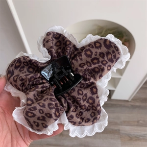 Macro detail of leopard print fabric claw clip with white lace trim and metal spring mechanism