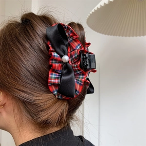 Red plaid bow hair claw clip with pearl accent on a woman's bun for Christmas