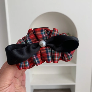 Close-up of tartan pattern bow hair clip with black satin and white pearl detail