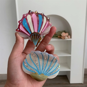 Detail of shell-shaped acetate hair clips featuring colorful stripes and sparkling rhinestones