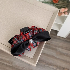 Close-up of red plaid bow hair claw clip with pearl accent on a beige display tray
