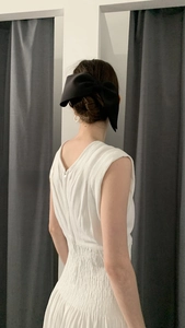 Close-up of a large black satin bow hair clip on a model in a white backless dress